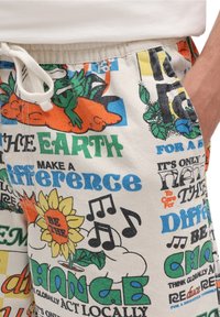 Shorts en coton avec un imprimé graphique coloré mettant en avant des fleurs, des notes de musique et des messages écologiques. Taille avec cordon de serrage et poches latérales.