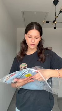 Sinised teksased, pakitud klaarsesse plastikkaussi. Teksadel on volditud disain ja neile on kinnitatud kollane hinnasilt.