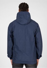 Chaqueta con capucha de color azul marino con una superficie texturizada, puños elásticos y un diseño de corte holgado. Capucha visible y detalles de costura en el collar.