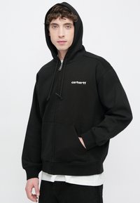 Sudadera con capucha negra con cierre de cremallera, hecha de mezcla de algodón, con capucha ajustable con cordón, bolsillos delanteros y logo blanco de Carhartt en el pecho izquierdo.