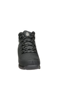 Zapatilla negra con parte superior de malla y puntera reforzada. Presenta una superficie texturizada, cordones redondos y un emblema de logo en la lengua.