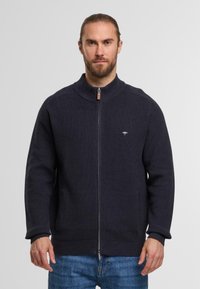 Marinefarbener Reißverschluss-Pullover aus Rippenstoff, mit hohem Kragen, Reißverschluss mit Holzakzent und kleinem Logo auf der Brust.