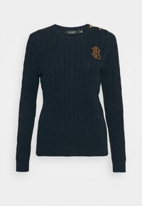 Marinblå stickad tröja med flätmönster, ribbade muddar och fåll, rund halsringning och en guldfärgad knappdetalj på axeln. Logotypaccent framtill.