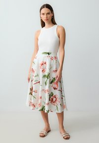 Weißes Sommerkleid mit rosa und grünen Blumenmustern, ausgestellter Schnitt, kombiniert mit einem weißen Tanktop und Sandalen mit Riemchen. Glatter Stoff.