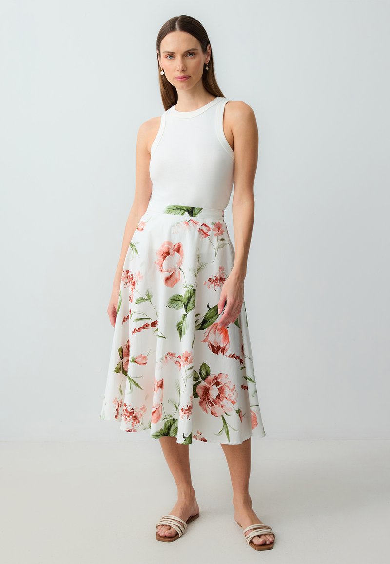 Weißes Sommerkleid mit rosa und grünen Blumenmustern, ausgestellter Schnitt, kombiniert mit einem weißen Tanktop und Sandalen mit Riemchen. Glatter Stoff.