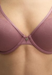 Mauve-BH mit Spitze, unterfütterten Cups und gewellten Kanten. Mit einem kleinen dekorativen Anhänger an der Vordermitte.