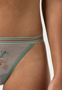 Culotte de bikini en mesh vert ornée de broderies florales, avec une taille rehaussée de rayures multicolores, mettant en valeur des détails fins.