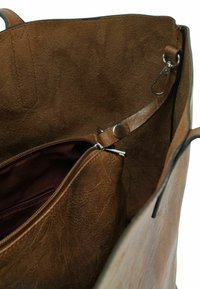 Interieur van een bruin lederen handtas met een zachte textuur, een ritsvak en een metalen sluiting. Het ontwerp is ruim met gladde randen.