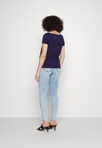 Top de manga corta navy combinado con jeans ajustados de lavado claro y tacones negros destalonados. Tejido suave, diseño ajustado y detalles sutiles en los jeans.