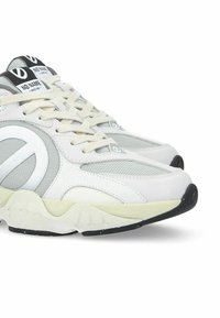 Sneakers atletici bianchi e grigi presentano materiali in rete e pelle, punta rotonda, dettagli testurizzati e una spessa suola in gomma.