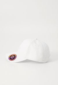 Hvid baseballcap med en afrundet krone, buet skygge, broderet logo og et farverigt mærketag på siden. Blødt stofs tekstur.