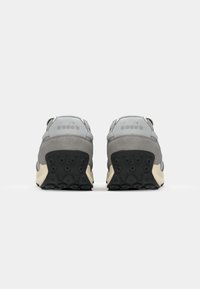 Baskets en suede gris et mesh avec une forme arrondie, semelle en caoutchouc noir présentant des textures circulaires, et un logo discret sur le talon.