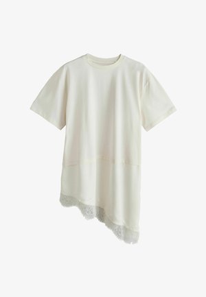 Lühikeste varrukatega helebeež kihiline top asümmeetrilise pitsiga ääristatud servaga ühtlasel taustal.