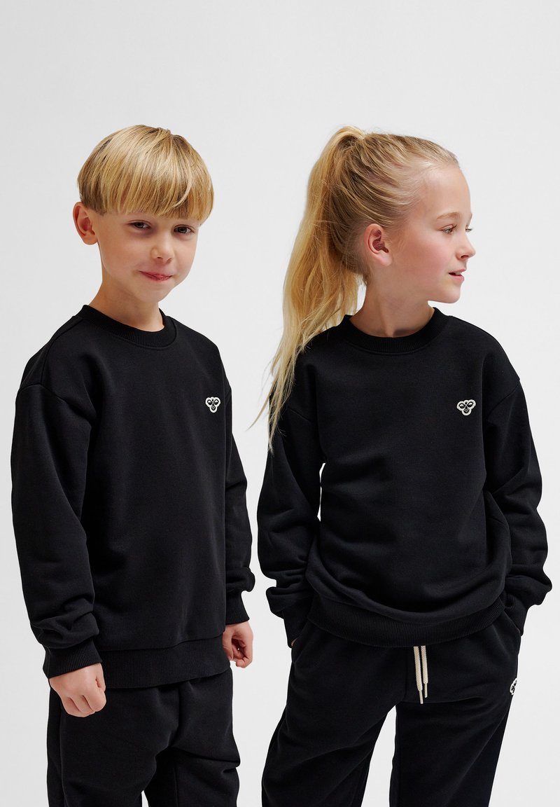 Svart sweatshirt i bomullsblandning med ribbade muddar och nederkant, med en liten broderad logga på vänster sida. Stylingen kompletteras med matchande byxor.