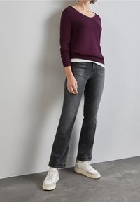 Burgundy v-ringad tröja, åtsittande, kombinerad med urtvättade grå raka jeans och vita sneakers. Släta texturer och avslappnad design.