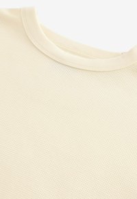 Tekstureret cremet skjorte med rund halsudskæring. Designet har et vaffelmønster og en blød, glat finish.