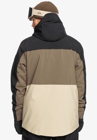 Veste imperméable pour homme avec un design tricolore : noir, khaki et crème ; dotée d'une capuche et d'un tissu texturé.