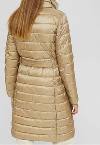 Beige Daunenjacke mit tailliertem Gürtel, horizontaler Steppung und hohem Kragen. Glattes, glänzendes Material mit minimalen Akzenten.