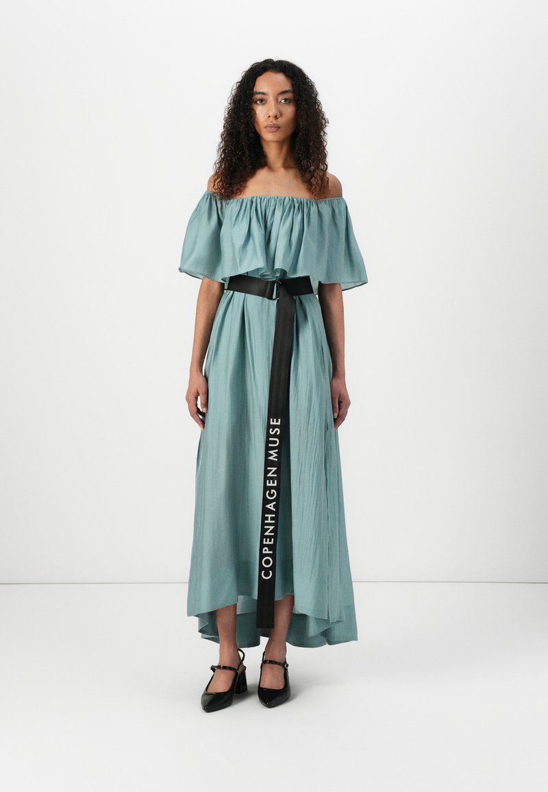Un lungo abito teal con scollatura a spalle scoperte e un design plissettato, stretto in vita con una cintura nera con il testo "COPENHAGEN MUSE".