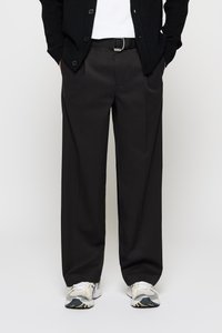 Black, wide-leg trousers with a smooth finish, featuring a flat front and belt loops. Paired with gray and white athletic shoes.