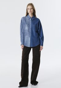 Camisa de mezclilla de dos tonos, clara de un lado y oscura del otro. Tiene un bolsillo en el pecho. Combinada con pantalones de pierna ancha de estampado de leopardo marrón.