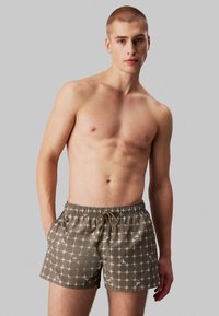 Bruine zwemboxers met een ruitpatroon en witte accenten. Beschikt over een elastische tailleband met verstelbaar trekkoord en zijzakken.