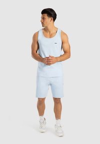 Hellblaues Tanktop und passende Shorts aus weichem Stoff. Verfügt über ein kleines Logo auf der Brust und eine lockere Passform. Schuhe: weiße Turnschuhe.