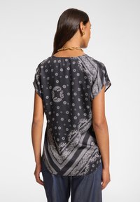 Top corto nero a maniche corte con motivi paisley bianchi e dettagli floreali. Tessuto leggero, vestibilità rilassata, presenta un orlo posteriore curvo.