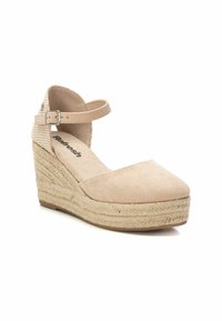 Zapato de cuña en color beige con parte superior similar al ante, correa al tobillo y suela de yute trenzado. Presenta una puntera redondeada y detalles texturizados en la correa.