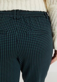 Pantalones con patrón de espiga en negro y verde azulado que cuentan con una cinturilla elástica, dos bolsillos traseros y un acabado texturizado.