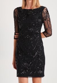 Svart kort klänning med genomskinliga trekvartärmar. Har intrikata paljettblommönster och pärldetaljer på en figurnära siluett.