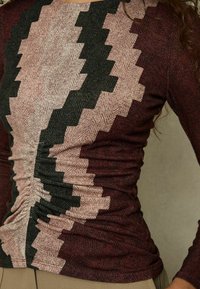 Top a maniche lunghe con motivo a zigzag in bordeaux, rosa e verde scuro; tessuto testurizzato; dettagli arricciati sui lati che aggiungono dimensione.
