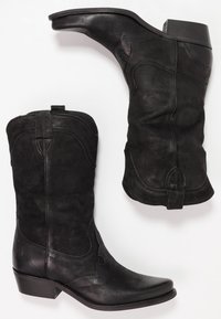 Para czarnych skórzanych kowbojskich butów z dekoracyjnym haftem, spiczastymi noskami, uchwytami oraz piętami na stosie na białym tle.