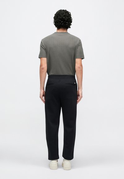 Pilkas trumpomis rankovėmis marškinėlis su tekstūruotu raštu, derinamas su juodomis siaurėjančiomis sportinėmis kelnėmis, pasižyminčiomis lygiu paviršiumi ir kišenėmis, matomas iš nugaros.