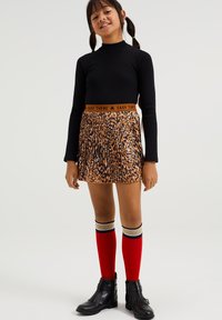 Melnas garas piedurknes krekls un plisēta svārki ar dzīvnieku apdrukas rakstu. Sarkanās ceļgalu augstās zeķes ar svītrojumiem un melni potīšu zābaki.