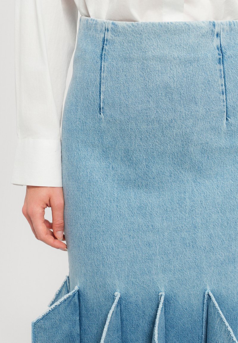 Lichtblauwe denimrok met een hoge taille, die een gestructureerd ontwerp benadrukt. Bevat zakken en franjes aan de zoom.