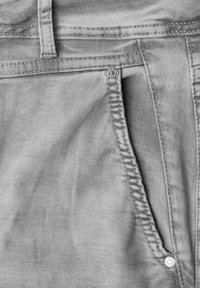 Gros plan sur un jean en denim gris montrant la poche avant, la boucle de ceinture, la couture et les rivets métalliques.