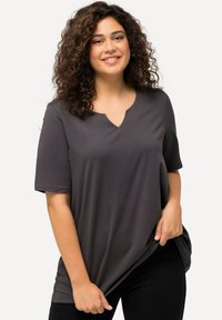 Maglietta grigia a maniche corte e scollatura a V, realizzata in tessuto morbido, con una vestibilità comoda e dettagli di cucitura discreti. Indossata con pantaloni scuri.