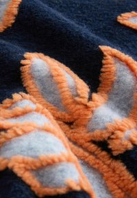 Nahaufnahme eines weichen marineblauen Stoffes mit strukturierter orange-grauer Blumenstickerei, die geschichtete Blütenblattformen bildet.