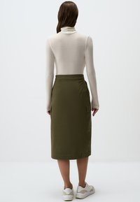 Olijfgroene midi-rok van duurzaam materiaal met zijzakken. Gestyled met een licht shirt met lange mouwen en witte sneakers. Eenvoudig ontwerp, praktisch.