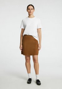 T-shirt bianco in cotone con una vestibilità comoda, abbinato a una gonna satinata marrone di lunghezza al ginocchio. Il modello indossa mocassini neri e calzini bianchi alla caviglia.