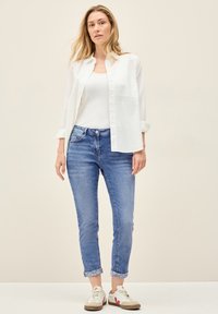 Vit skjorta, vit linne, ljusblå jeans med uppvikta cuffs och beiga sneakers med röda detaljer. Slät textur och avslappnad passform.