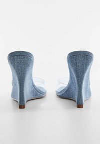 Sandali con tacco alto in denim, con cinturini trasparenti, forma curvata e finitura texturizzata. Presentano una base solida e un design con tacco largo.