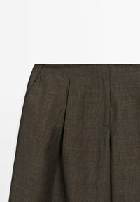 Mörkbrun linneskjort med veck, som har en smidig textur och ett rent, strukturerat midjeband. Minimalistisk design utan synlig hårdvara.