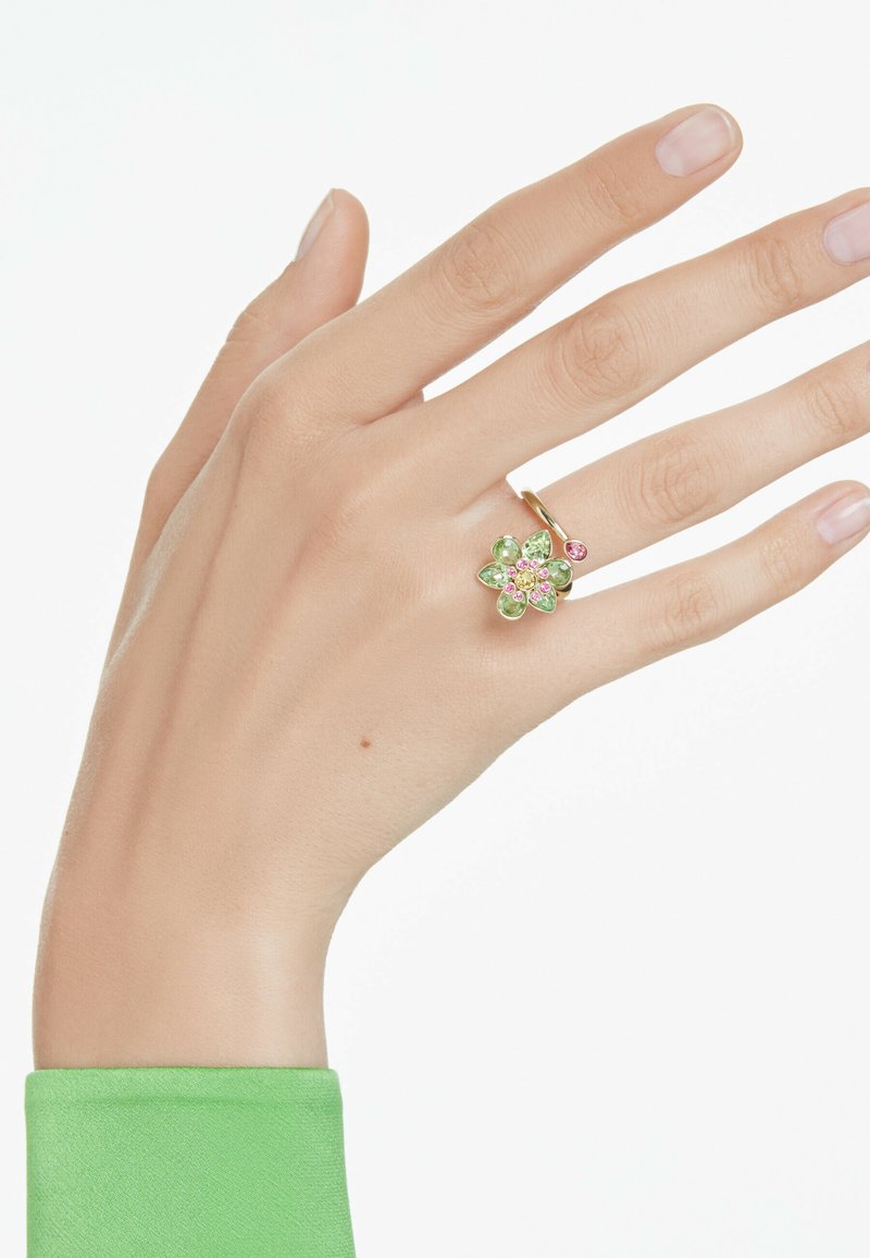 Gold ring featuring a floral design with green and pink gemstones, displaying a polished texture and delicate petals. Hand positioned gracefully.