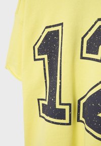 Tissu jaune avec un grand numéro noir "12" imprimé, présentant une texture tachetée et vieillie sur les chiffres.