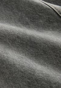 Gros plan sur un tissu en denim gris montrant la texture en sergé diagonal et une couture dans le coin supérieur droit.