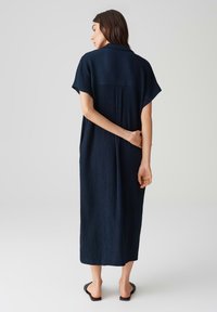 Abito maxi blu navy in tessuto testurizzato, con maniche corte e una vestibilità morbida, caratterizzato da una cucitura sul retro e un orlo leggermente curvo.