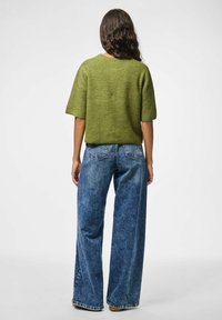 Pull en tricot vert olive à manches courtes, associé à un jean en denim bleu ample. Le pull présente une surface texturée et une coupe décontractée.