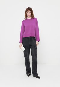 Pull en tricot violet avec un col rond et un ourlet côtelé, associé à un pantalon cargo noir avec de grandes poches latérales et un petit sac argenté élégant.